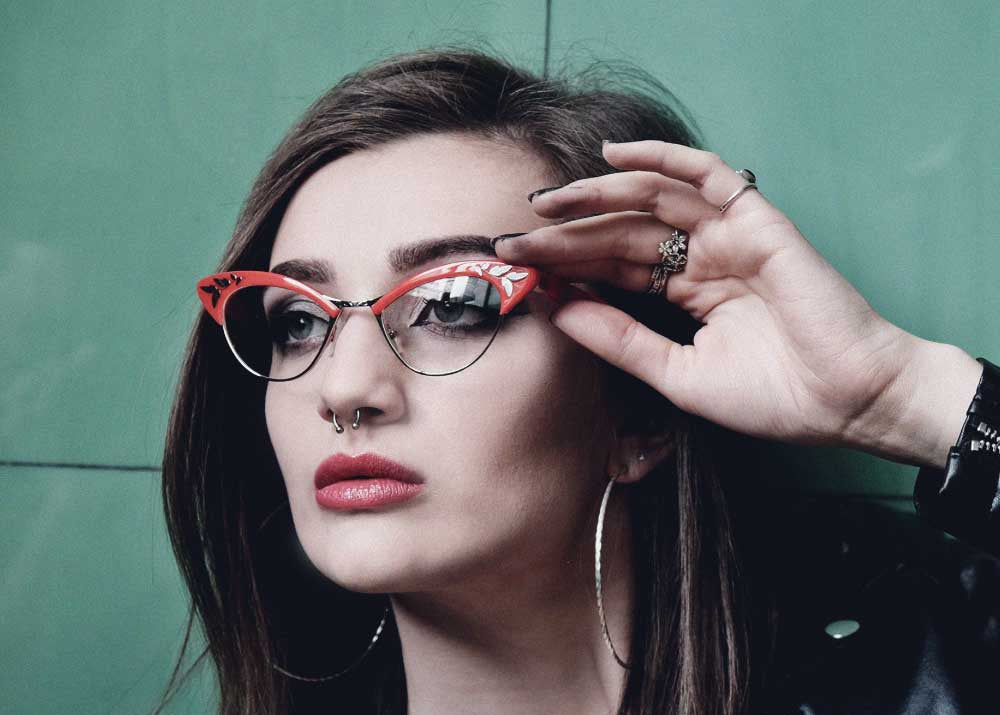 Woman adjusting red cat-eye glasses against a green background