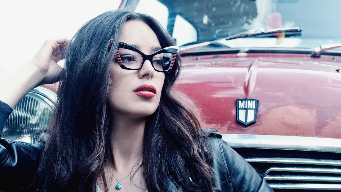Model sat infront of a red mini car wearing dramtic cat-eye glasses