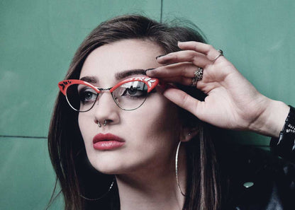 Woman adjusting red cat-eye glasses against a green background