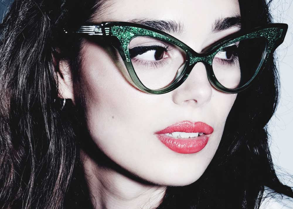 Woman wearing green glittery cat-eye glasses with a black and white background