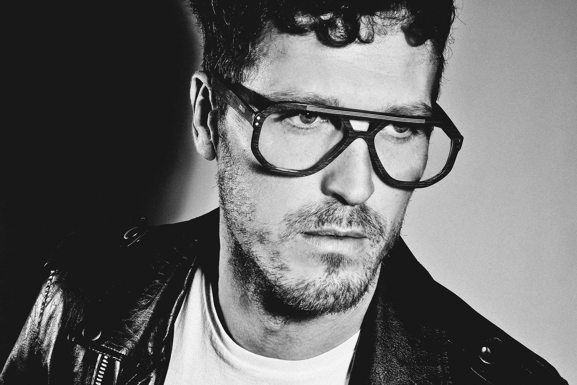 Man wearing a leather jacket and glasses in black and white.