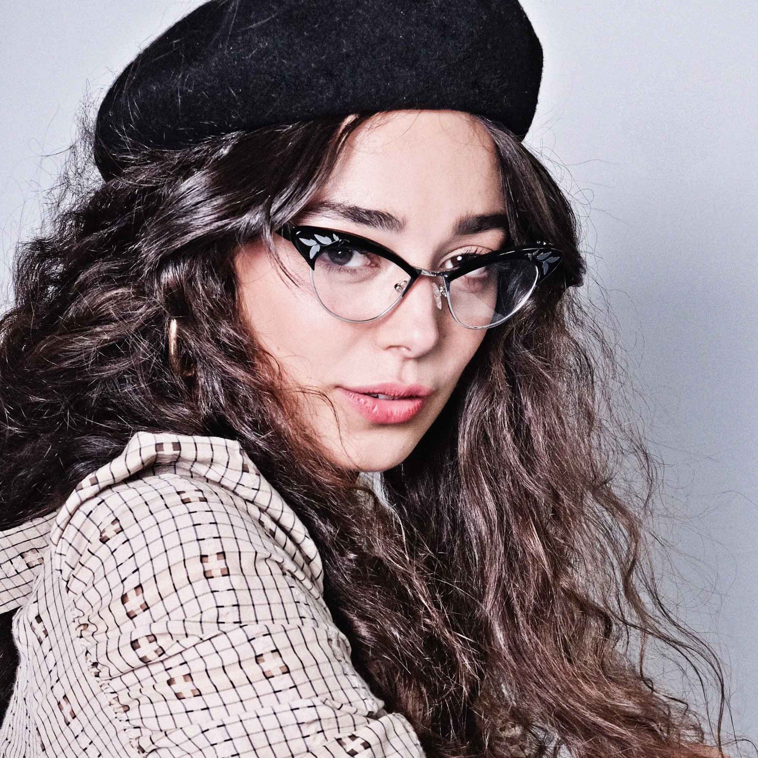 Model wearing a black beret and black and silver cat eye glasses frames.